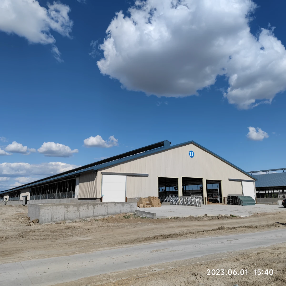 Steel dairy barn with large sliding doors and open ventilated sides, repeated across a large farm