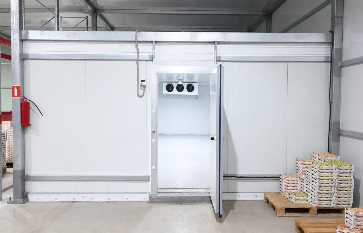 Insulated cold room door open on a fruit storage room — door cycles drive infiltration load