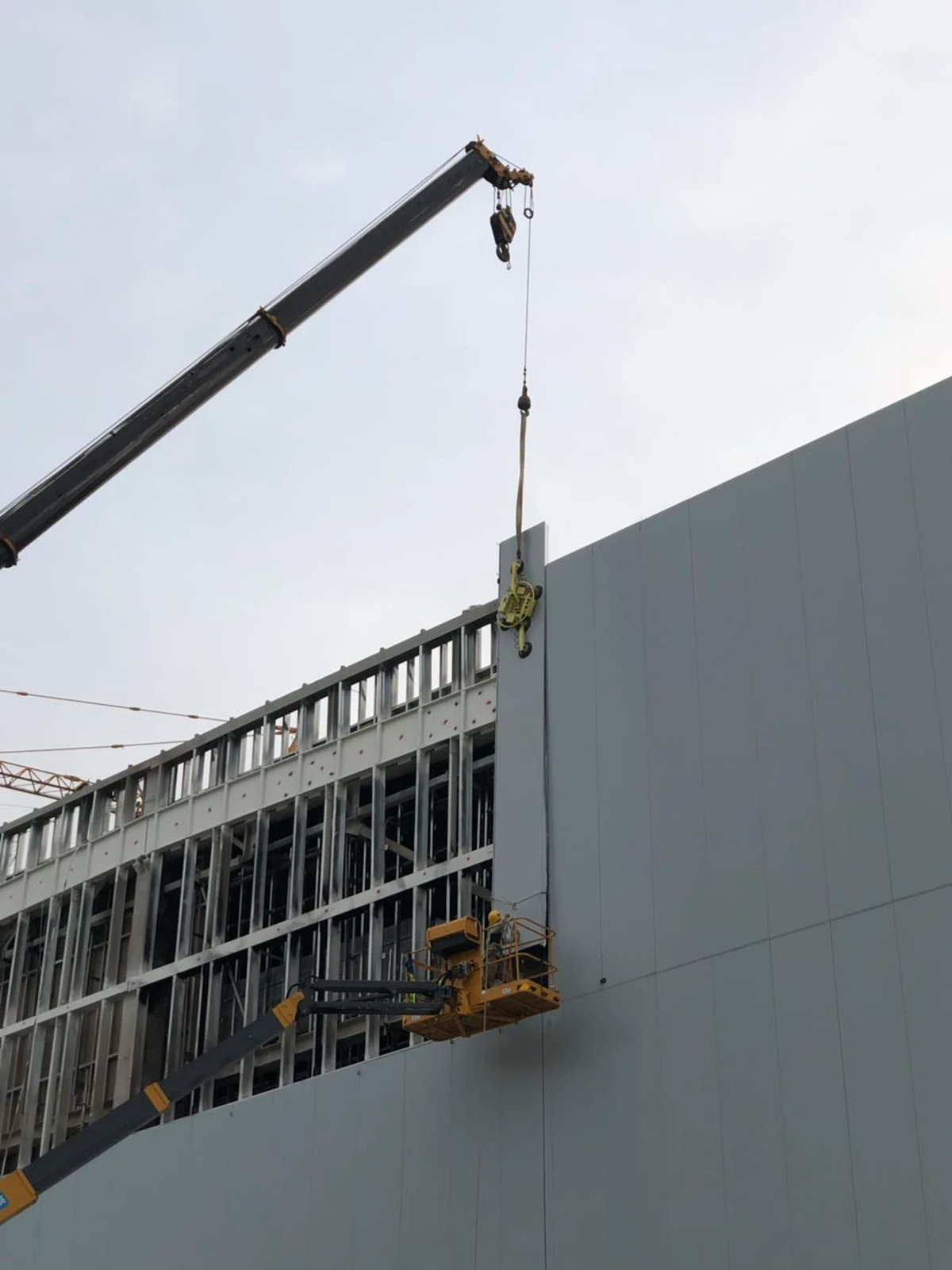 Large insulated wall panel being lifted by crane onto an industrial steel building frame by Vikkins